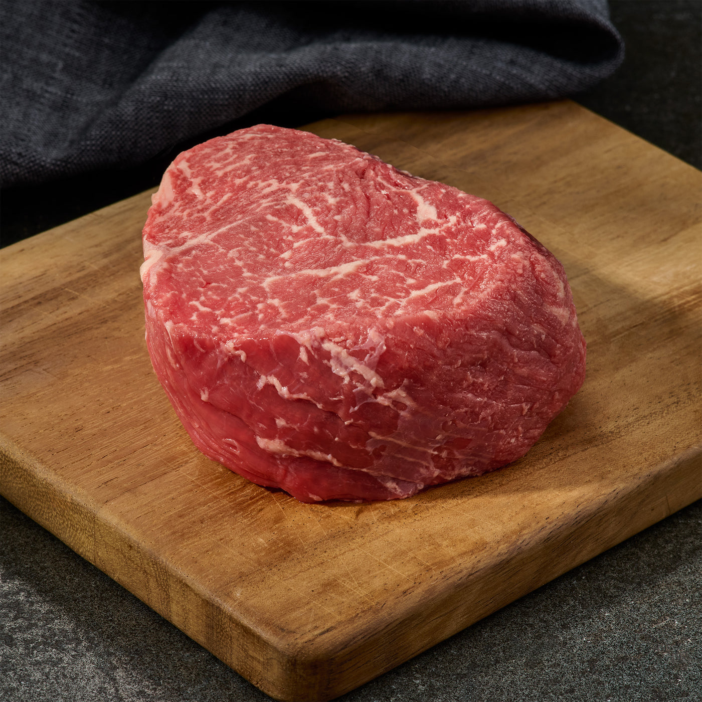 Raw top sirloin steak on a wooden cutting board with a dark background