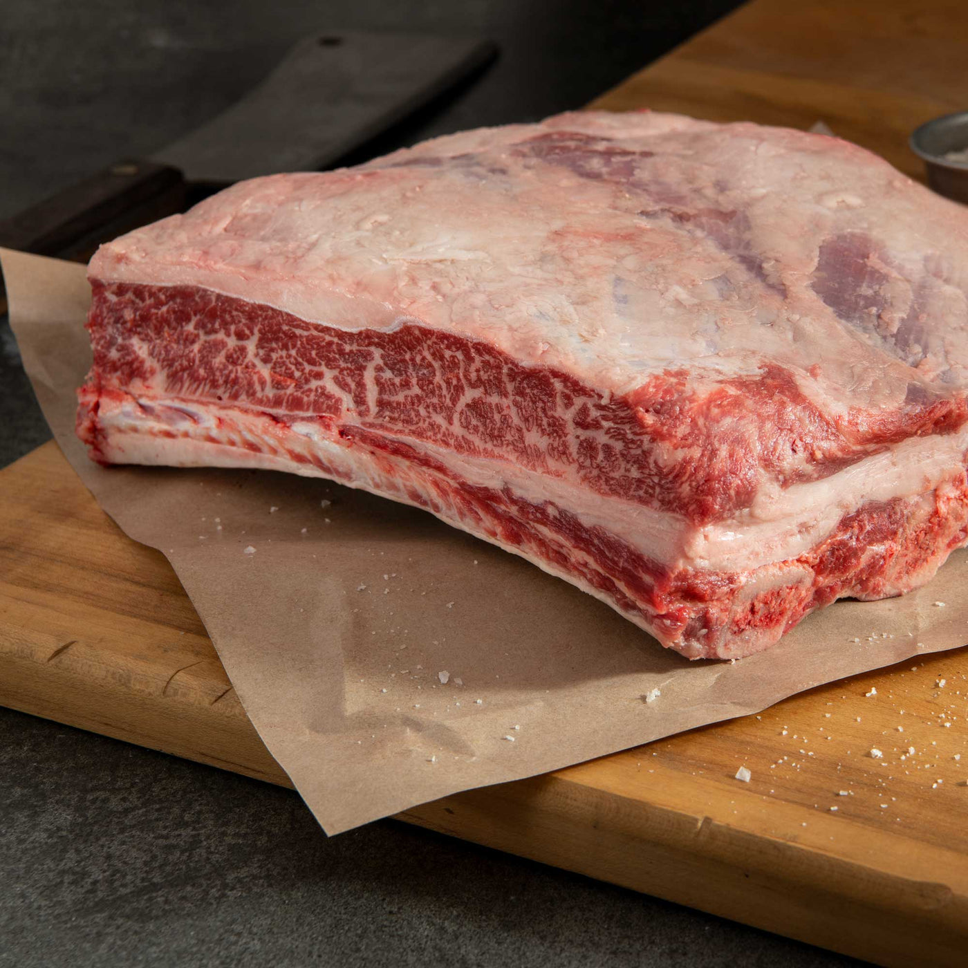 A bone-in short rib plate NAMP123A cut resting on a piece of parchment paper spread out on a wooden cutting board, showcasing the marbled red meat.