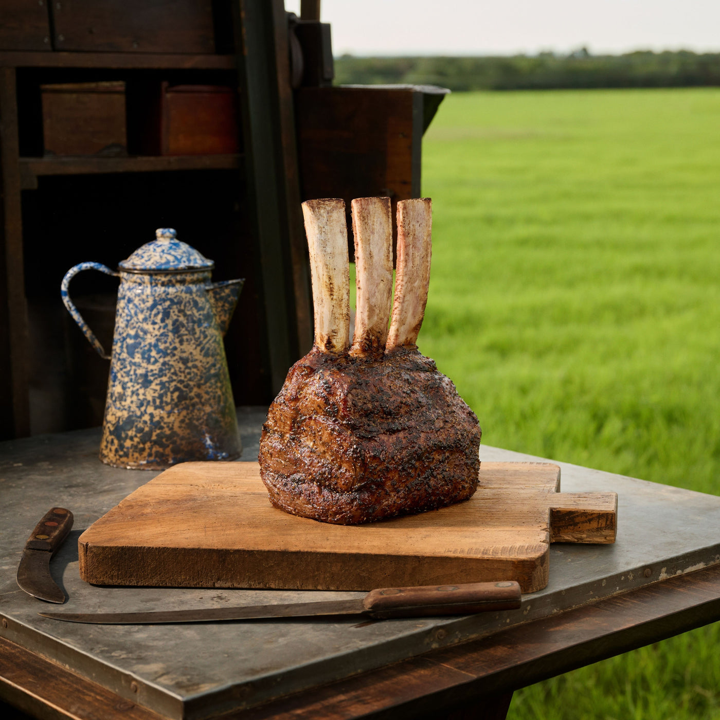 Tomahawk Prime Rib on a wooden cutting board with a rustic setting and open field in the background
